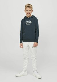 Felpa blu scuro con logo bianco, abbinata a pantaloni della tuta grigio chiaro e scarpe da ginnastica bianche. Tessuto morbido, vestibilità comoda e cappuccio con coulisse.
