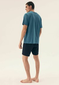 Turkusowa bawełniana koszulka z krótkim rękawem w połączeniu z granatowymi szortami. Gładka faktura, prosty design i brak widocznych wzorów lub elementów metalowych.
