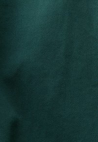 Zelená texturovaná tkanina se geometrickým vzorem, s hladkým povrchem a mírným leskem. Materiál se zdá být odolný a pevně tkaný.