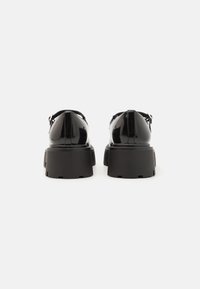 Black patent leather shoes with a chunky, textured sole. Rounded toe and adjustable strap detailing at the heel.