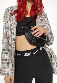 Svart läder axelväska med silverdetaljer, rutig skjorta i pastellfärger, svart sportbh och svarta leggings med vit logoband.