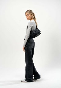 Borsa a tracolla nera con più scomparti impilati, realizzata in materiale testurizzato. Maglia grigia a maniche lunghe, jeans scuri a vita alta e sneakers.