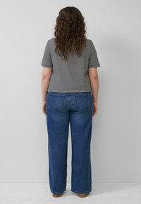 Gestreiftes Kurzarmhemd in Schwarz und Weiß, kombiniert mit weiten blauen Jeans. Beide Kleidungsstücke haben einen entspannten Schnitt.