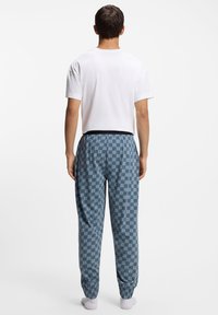 Witte korte mouw t-shirt gecombineerd met blauwe joggerbroek met patroon. De broek heeft een geometrisch ontwerp en een elastische tailleband.