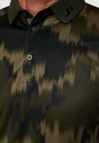 Kortärmad pikétröja i mörkgrön och svart med ett texturerat, vågigt mönster. Har en knapp-down krage och embossad logotyp på kragen.