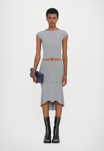 Top de punto gris con canalé, mangas cortas y corte; falda midi a juego con dobladillo acampanado. La modelo sostiene un bolso azul texturizado y lleva botas negras.