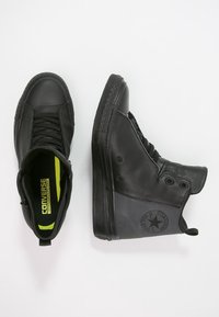 Schwarze High-Top-Sneaker mit einem glatten Leder-Obermaterial, kontrastierenden matten und glänzenden Abschnitten sowie einem auffälligen Logo-Patch an der Seite.