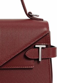 Sac à main structuré bordeaux avec surface texturée, quincaillerie argentée et fermeture à rabat. Doté d'une bandoulière en boucle et d'un détail de boucle décoratif.