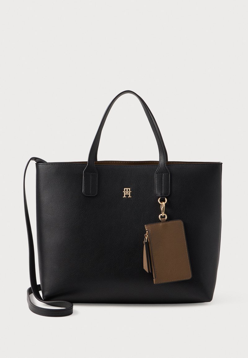 Sort læder tote bag med dobbelte håndtag, der har et guld logo og en aftagelig brun kortholder som accent. Glat tekstur, struktureret form.