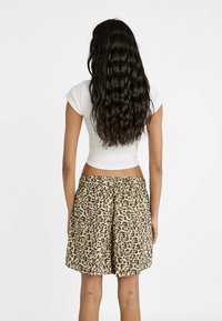 Leopardenmuster-Shorts mit einem elastischen Bund, beigem Hintergrund und schwarz-braunen Flecken. Getragen mit einem engen weißen Oberteil. Glattes Material.