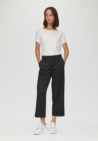 Chemisette blanche à manches courtes associée à un pantalon cropped texturé noir. Le modèle porte des baskets compensées blanches. Design simple et moderne.
