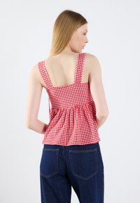 Rød og hvid gingham ternet ærmeløs top, tætsiddende skrog med gathered talje, glat stof, firkantet udskæring, vist med mørke jeans.