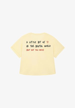 Geel katoenen T-shirt met korte mouwen en een ronde halslijn. Tekst op de achterkant in zwart en rood luidt: "Een beetje ❤️ in deze brute wereld (maar niet te veel)."