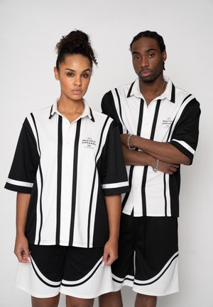 Two serious young adults wearing matching black and white vertically striped shirts and shorts, standing against a plain background.