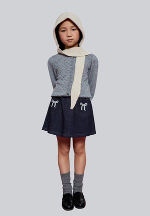 Cárdigan acolchado gris con botones, falda vaquera con bordado de lazo, bufanda beige con capucha, calcetines grises hasta la rodilla y zapatos negros.