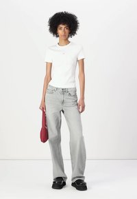 T-shirt bianca a maniche corte, jeans a vita alta grigio chiaro, scarpe platform nere chunky e una borsa rossa con un design curvo.