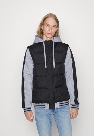 Sort pufferjakke med en grå hætte sweatshirt, stribede manchetter og forlommer. Tekstureret stof med en tætsiddende design.