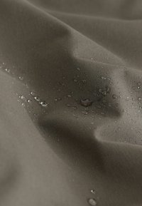 Water droplets resting on brown fabric, showing texture and water resistance with slight wrinkles and folds.
