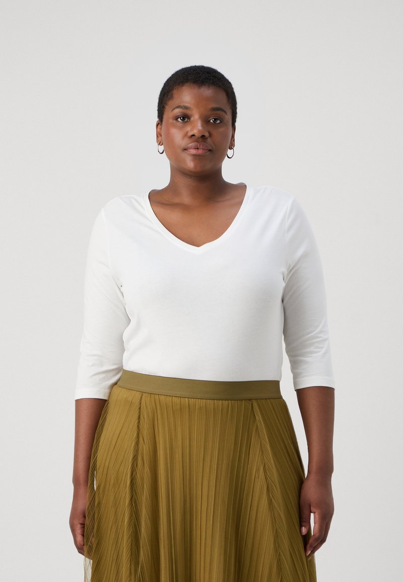 Top branco, justo, de manga três quartos com decote em V. Combinado com uma saia longa, plissada, verde-azeitona com uma cintura larga.