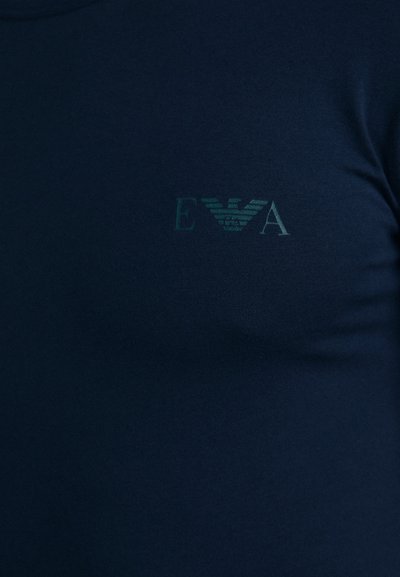 T-shirt bleu marine arborant un subtil emblème vert avec les lettres "EVA" et un motif d'aile, fabriqué en tissu doux et extensible.