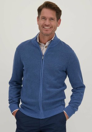 Blauwe zip-up trui met een textuurdesign, uitgerust met geribde manchetten en zoom. Draag het over een geruit shirt, weergegeven tegen een effen achtergrond.