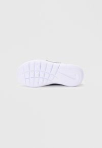 Semelle extérieure de chaussure de sport noire, en caoutchouc blanc texturé avec un motif de traction, arborant un logo proéminent et des rainures pour la flexibilité.