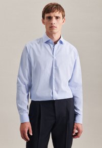 Camicia a quadri blu chiaro con colletto a bottone, maniche lunghe e design aderente. Il tessuto appare liscio con una sottile texture.