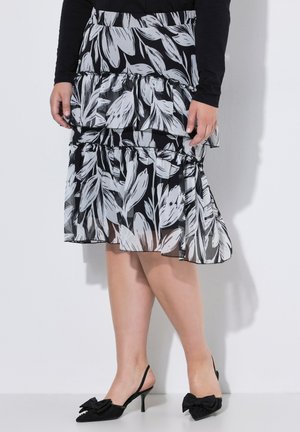 Czarna i biała kwiecista spódnica z falbankami noszona z czarną bluzką z długim rękawem i czarnymi czółenkami typu slingback z kokardkami na palcach.