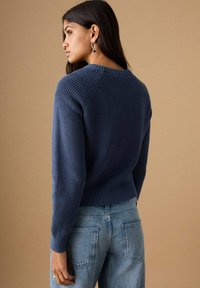 Mornarsko plavi pleteni džemper s rebrastom teksturom, okruglim izrezom i krojenim rubom, uparen s svijetloplavim trapericama.