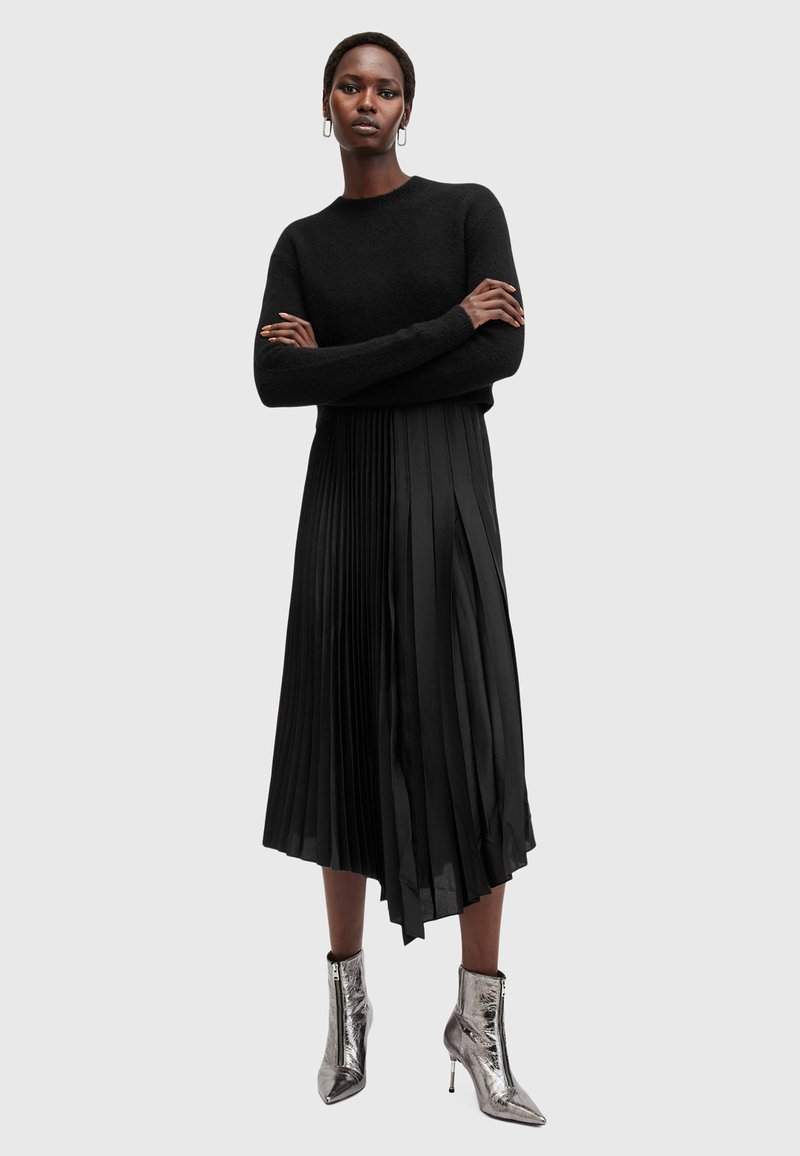Sort strikket sweater med lange ærmer, parret med en plisseret sort nederdel og metalliske ankelstøvler. Glat tekstur med en tætsiddende silhuet.