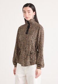 Blouse met luipaardprint en hoge kraag, zwarte knopen en een getailleerde taille. Lange, gepofte mouwen met zwarte accenten. Glad stoftextuur.