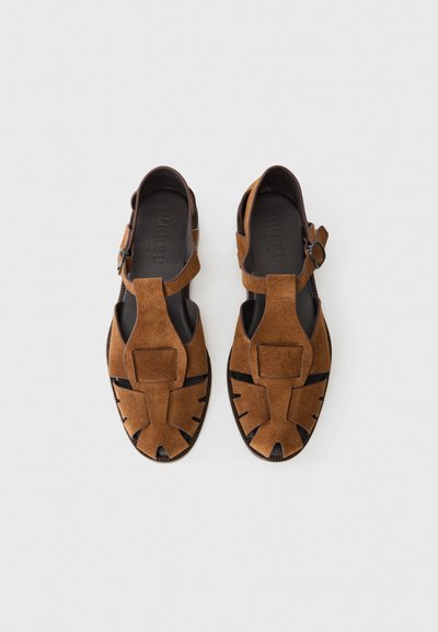 Sandales en daim marron avec un design à lanière en T, des découpes et un accent de boucle. Surface texturée et style ouvert.