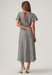 Black and white checked dress with a flared design, tied back neckline, short sleeves, and a mid-length hemline, made from lightweight fabric.