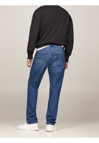 Blå jeans i denim med rakt ben och bakfickor samt en subtil blekt finish. Bärs med en svart sweatshirt och vita sneakers.