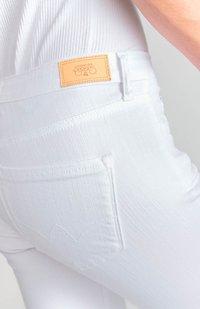 Jeans de mezclilla blanca con una etiqueta de cuero en la cintura y un diseño sutil en el bolsillo trasero con detalles de costura. Textura suave.