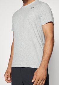 Camiseta gris de manga corta en tejido suave y transpirable con cuello redondo y un pequeño logo negro de Nike en la parte superior izquierda del pecho.