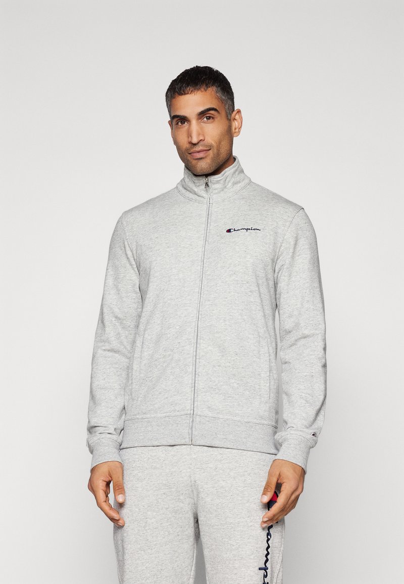 Gray zip-up sweatshirt with a high collar, ribbed cuffs, and a small embroidered logo on the left chest. Soft, textured fabric.