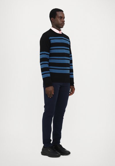 Pull noir avec des rayures bleues, associé à une chemise à col rose clair, un pantalon marine et des baskets noires. Design simple, coupe ajustée.