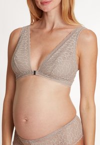 Lace bralette i taupe med en dyp V-hals, brede stropper og en frontlukking med en sølvdetalj, sammen med matchende blonde truser.