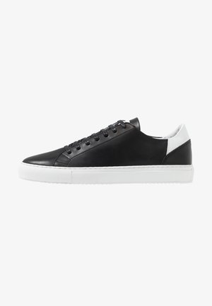 Black leather sneakers with a white rubber sole, featuring a smooth texture, round toe, and black laces. Subtle white accent at the heel.