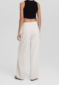 Vidbenade krämfärgade byxor i mjukt tyg, med hög midja, bakfickor och skräddarsydd design. Inga synliga mönster eller dekorationer.