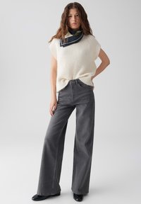 Lichtcrème oversized trui met korte mouwen, gecombineerd met hoog-taille, wide-leg donkergrijze jeans. Een nekdoek voegt contrast toe met marineblauwe accenten.