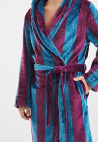 Pluszowy szlafrok z naprzemiennymi pionowymi paskami w kolorze niebieskim i burgundowym, z zamkniętym krojem, paskiem wiązanym i bocznymi kieszeniami. Miękka faktura.