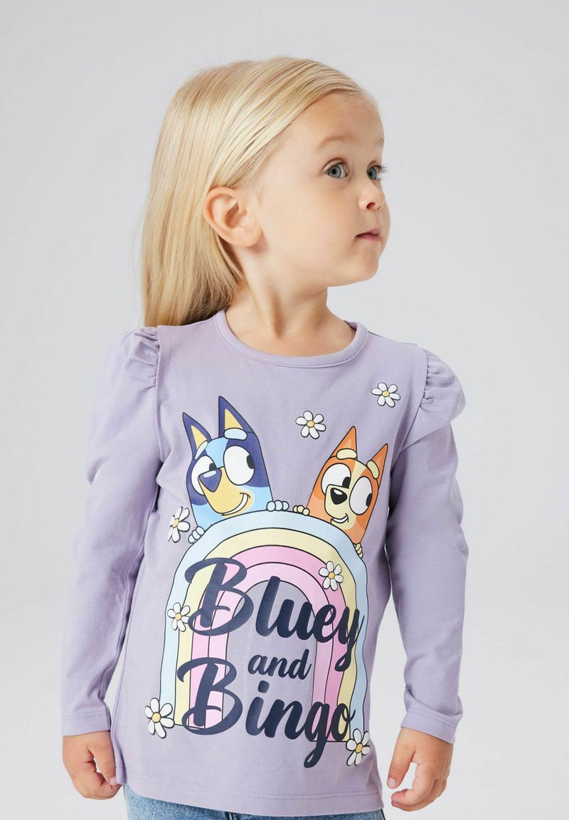 Lawendowa koszulka z długim rękawem z kolorową grafiką dwóch kreskówkowych psów, "Bluey" i "Bingo", z kwiatowymi akcentami i tęczowym wzorem.