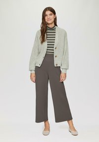 Lichtgrijze gebreide cardigan met grote knopen, gecombineerd met een donkergrijze high-waisted broek met wijde pijpen en een gestreepte coltrui.