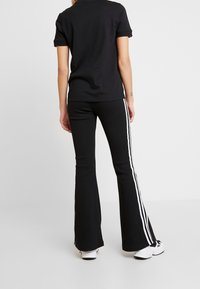 Svart kortärmad polo skjorta i kombination med svarta utsvängda byxor med vita sidostreifen. Bärs med vita sportskor.