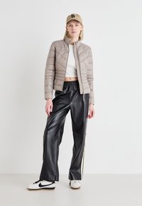 Beige quiltet jakke med høy krage, hvit crop top, svarte faux skinnbukser med sidestriper og hvite Nike-sneakers. Beige caps.