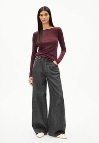 Bordeauxrotes Langarmshirt kombiniert mit weitem dunkelgrauen Jeans. Die Jeans haben eine hohe Taille und seitliche Taschen. Die Schuhe sind cremefarben.