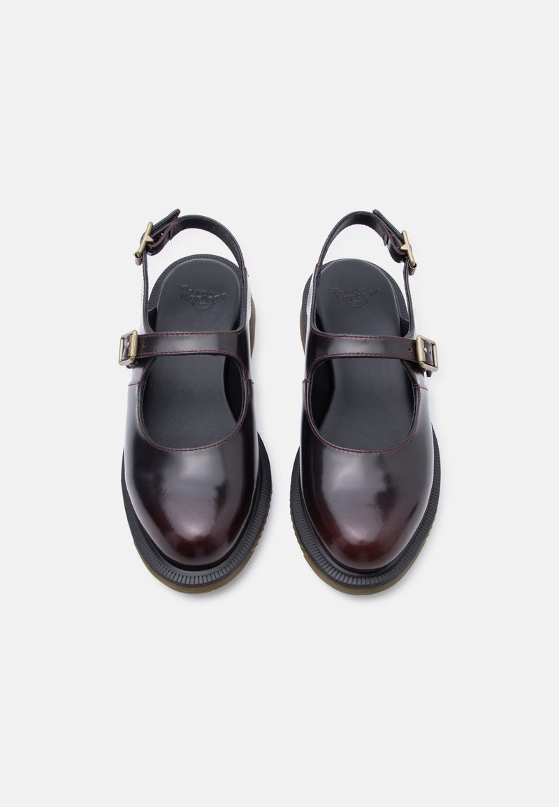 Coppia di scarpe Mary Jane lucide di colore marrone scuro con cinturini regolabili con fibbia e solette imbottite nere su sfondo bianco.