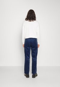 Modré manšestrové kalhoty s rovný střihem, s texturovaným povrchem, jemnými detaily zadních kapes a v kombinaci s černými botami.